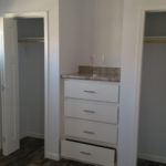 Image of standard dual closet setup with dresser in the middle. TV jack over dresser, and white bi-fold closet doors are standard. Closets come standard with shelf and rod.